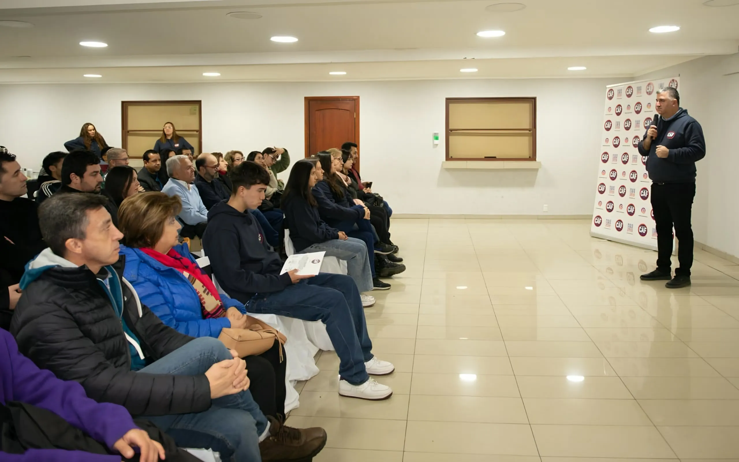 Charla educativa en un salón, con el público sentado escuchando al expositor.