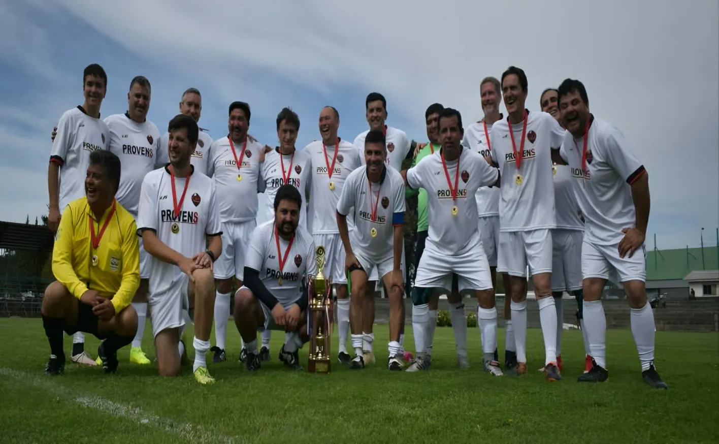 Equipo de fútbol adulto posando en la cancha con medallas, en una actividad de aniversario de la fundación.