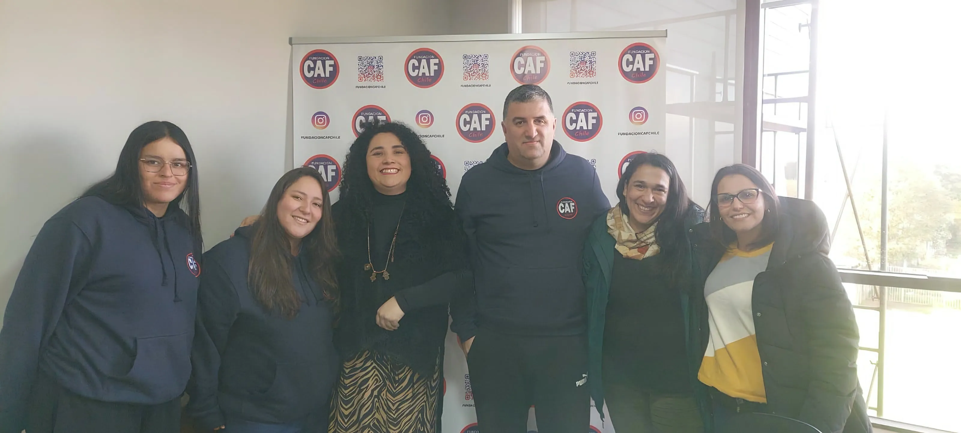 Grupo de seis personas adultas posando frente al telón de la fundación.